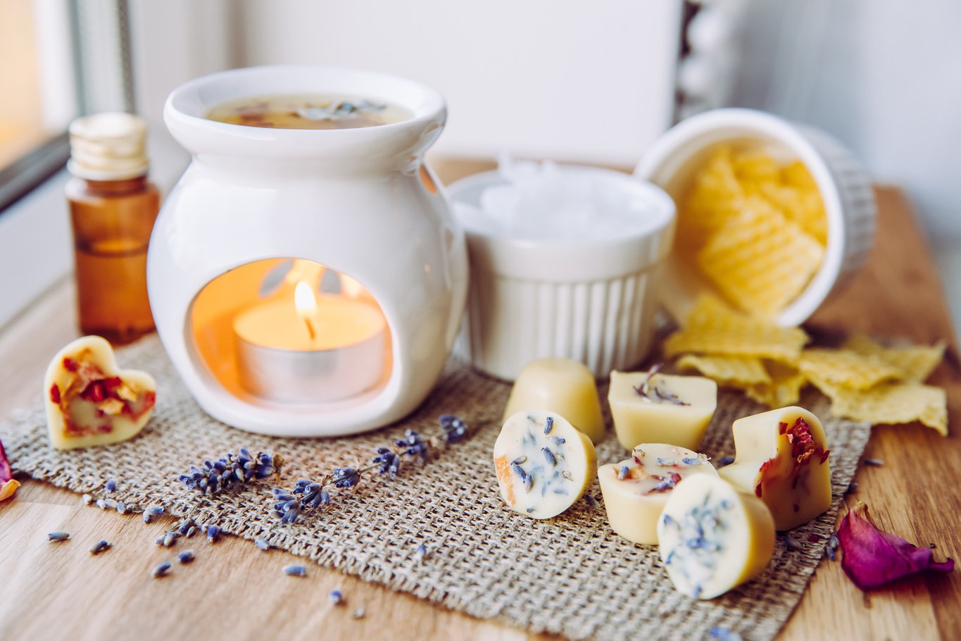 Using homemade mini wax melts in aromatherapy lamp diffuser at home interior concept. Melts making ingredients on table for unbleached beeswax, solid coconut oil, essential oil, dried flowers.